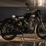 2026 Royal Enfield Classic 350 in black with gold detailing parked indoors in a sunlit industrial setting.