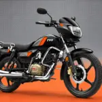 Black TVS Radeon motorcycle with orange accents, chrome details and alloy wheels against a grey and orange studio background.