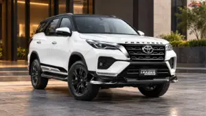 White 2026 Toyota Fortuner Leader Edition with black alloy wheels, a black roof and bold front grille outside a modern building.
